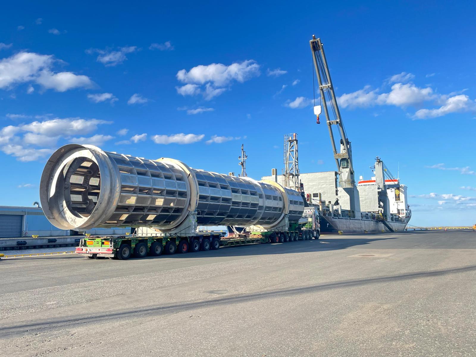 Erikoiskuljetus lastaamassa suurikokoista teollisuusosaa satamassa, Kuljetus Koiviston kuljetuskalusto ja rahtilaiva taustalla.